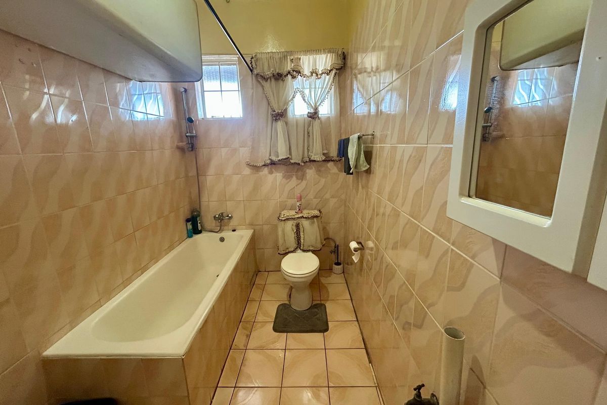A dated bathroom featuring full-height wall tiling, a standard bathtub, and a toilet, offering potential for a modern renovation.