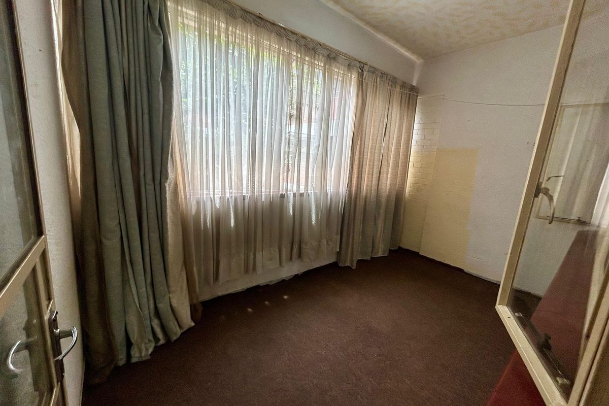 An empty bedroom featuring large windows, carpet flooring, and a textured ceiling, currently requiring cosmetic updates and wall repairs.