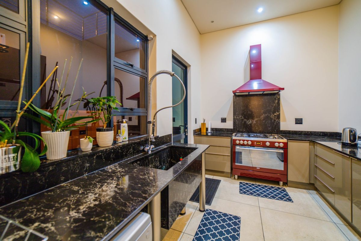 Modern kitchen featuring dark granite countertops, a large undermount sink with gooseneck faucet, and a striking red freestanding gas stove with matching extractor fan.