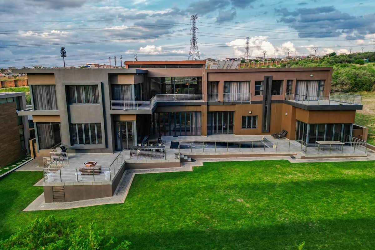 Aerial view of a modern multi-story residence featuring a large lawn, swimming pool, and multiple elevated balconies with contemporary architectural design.