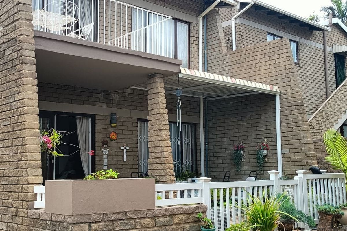 Rear view of a multi-level apartment building featuring a ground-floor patio and an upper-level balcony with brick facade finishes.