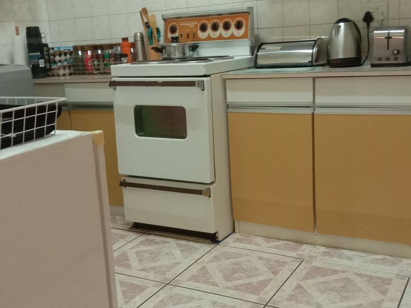 A dated kitchen featuring original cabinetry, a freestanding stove, tiled backsplash, and tiled flooring, offering potential for a modern renovation.