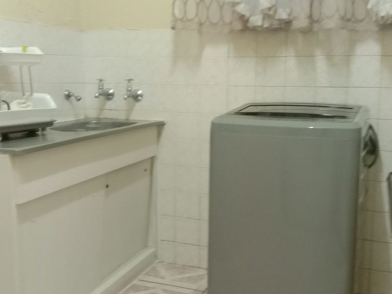 A functional laundry area featuring tiled walls, a stainless steel sink, and built-in cabinetry, offering a practical space for utility and washing needs.
