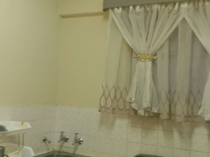 A functional kitchen area featuring a tiled splashback, stainless steel sink, and window with curtains.