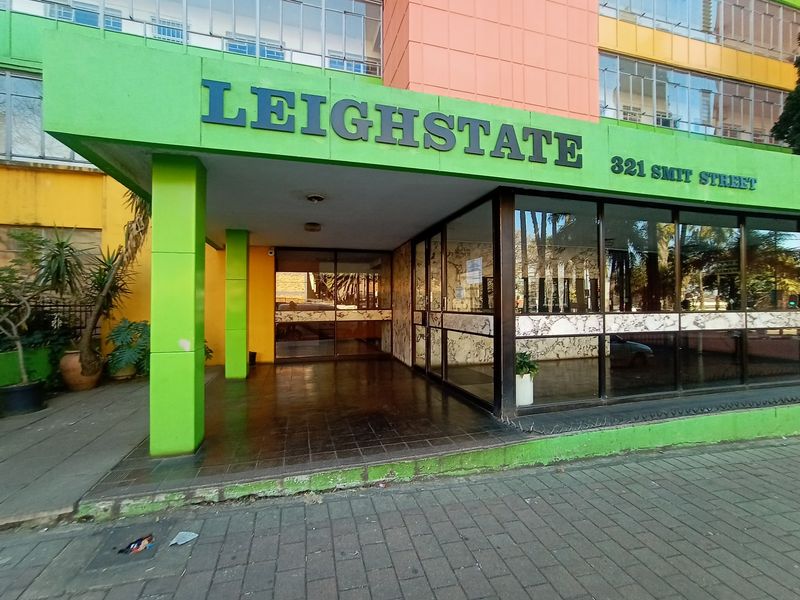 The front entrance of Leighstate apartment building, featuring a covered walkway, glass facade, and prominent street-level signage.