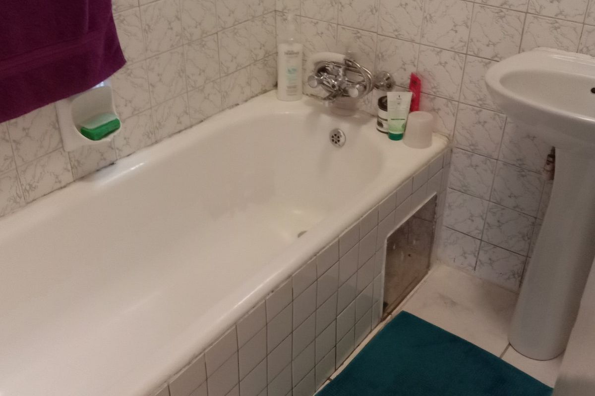 A compact bathroom featuring a standard bathtub with tiled apron and a pedestal basin, currently showing signs of wear and missing tile finish.