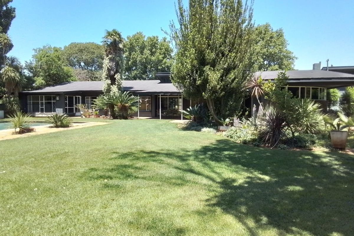A spacious rear garden featuring a well-maintained lawn, mature landscaping, and a swimming pool adjacent to the covered patio area.