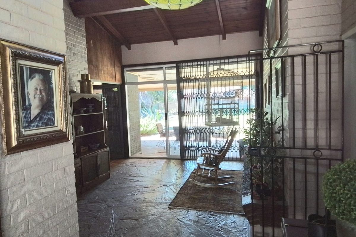 Living area featuring exposed timber ceiling beams, painted brick walls, and flagstone flooring, with direct access to the rear patio through sliding glass doors.