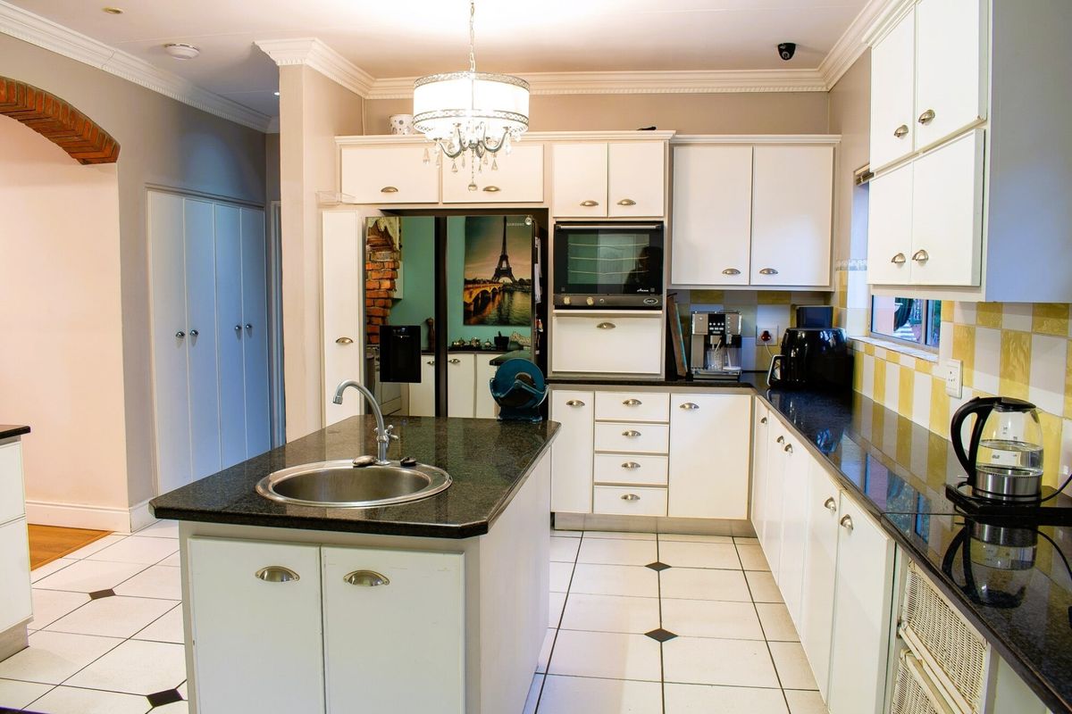 A well-maintained kitchen featuring white cabinetry, dark granite countertops, a central island with a sink, and classic tiled flooring.