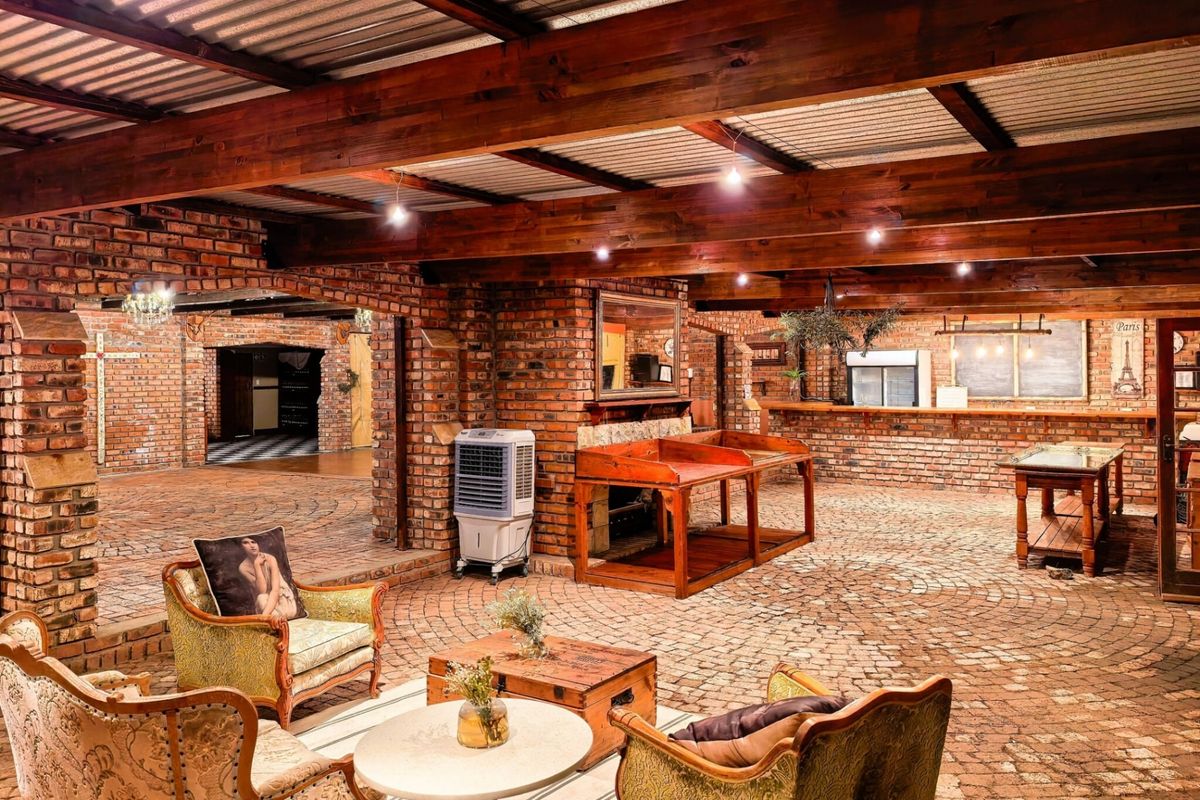 Spacious living area featuring rustic exposed brick walls, timber ceiling beams, and unique brick paved flooring, creating a warm and character-filled entertainment space.