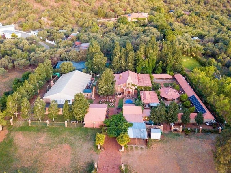 Aerial view of a large property featuring multiple buildings, a swimming pool, solar panels, and extensive landscaped grounds in a rural setting.