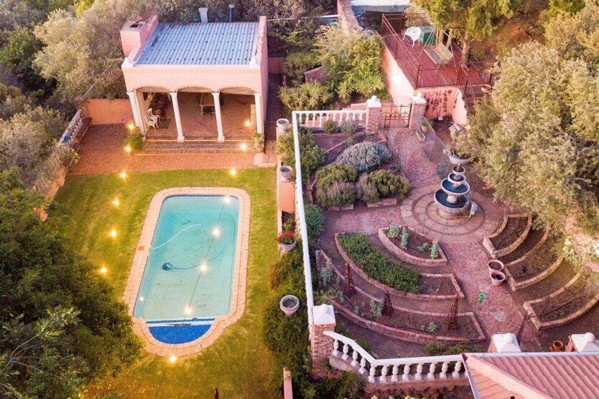 Aerial view of a landscaped garden featuring a swimming pool, a covered patio area, and a tiered garden with a central stone fountain.