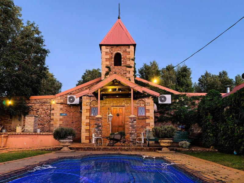 A charming rear exterior view featuring a unique brick tower, covered patio area, and a swimming pool set within a landscaped garden.