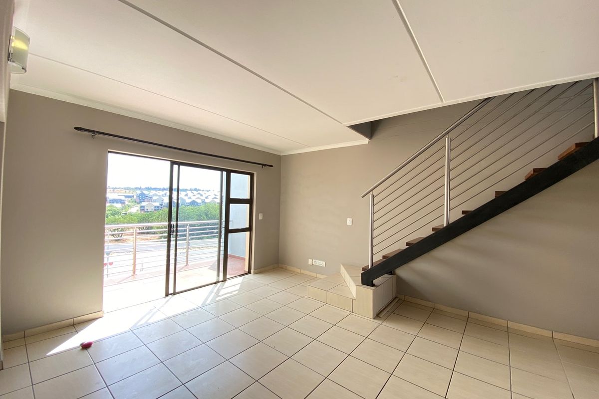 Spacious open-plan living area featuring neutral tiled flooring, a staircase with modern metal railing, and sliding door access to a private balcony.