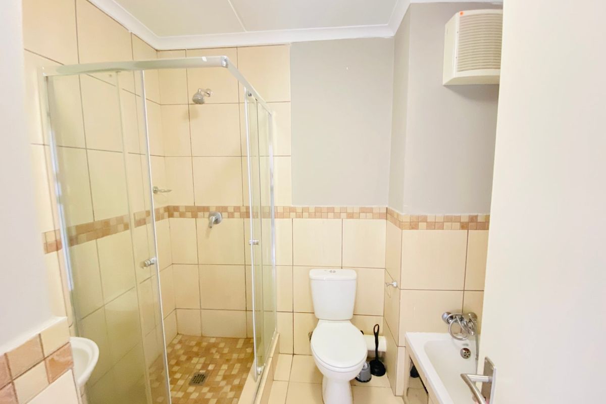 A functional bathroom featuring a glass-enclosed shower, toilet, and basin with neutral wall and floor tiling.