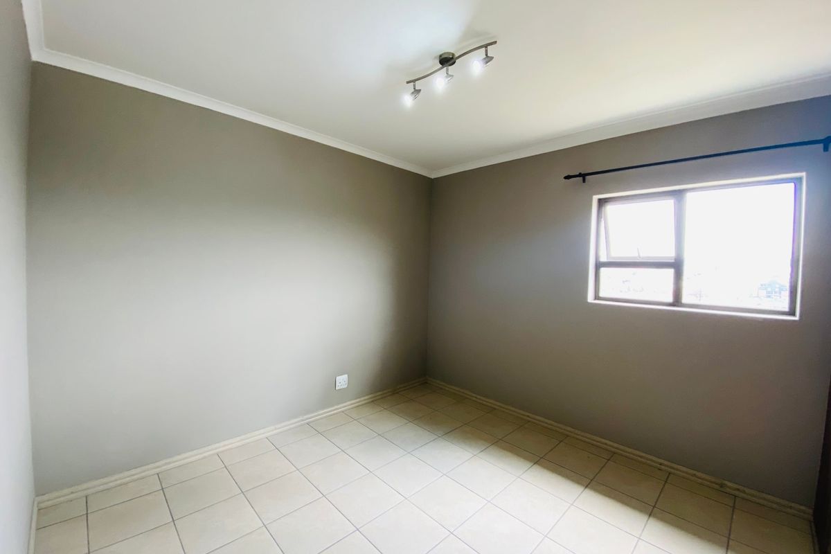 A clean, empty bedroom featuring neutral wall paint, tiled flooring, and a modern ceiling-mounted spotlight fixture, ready for personalization.