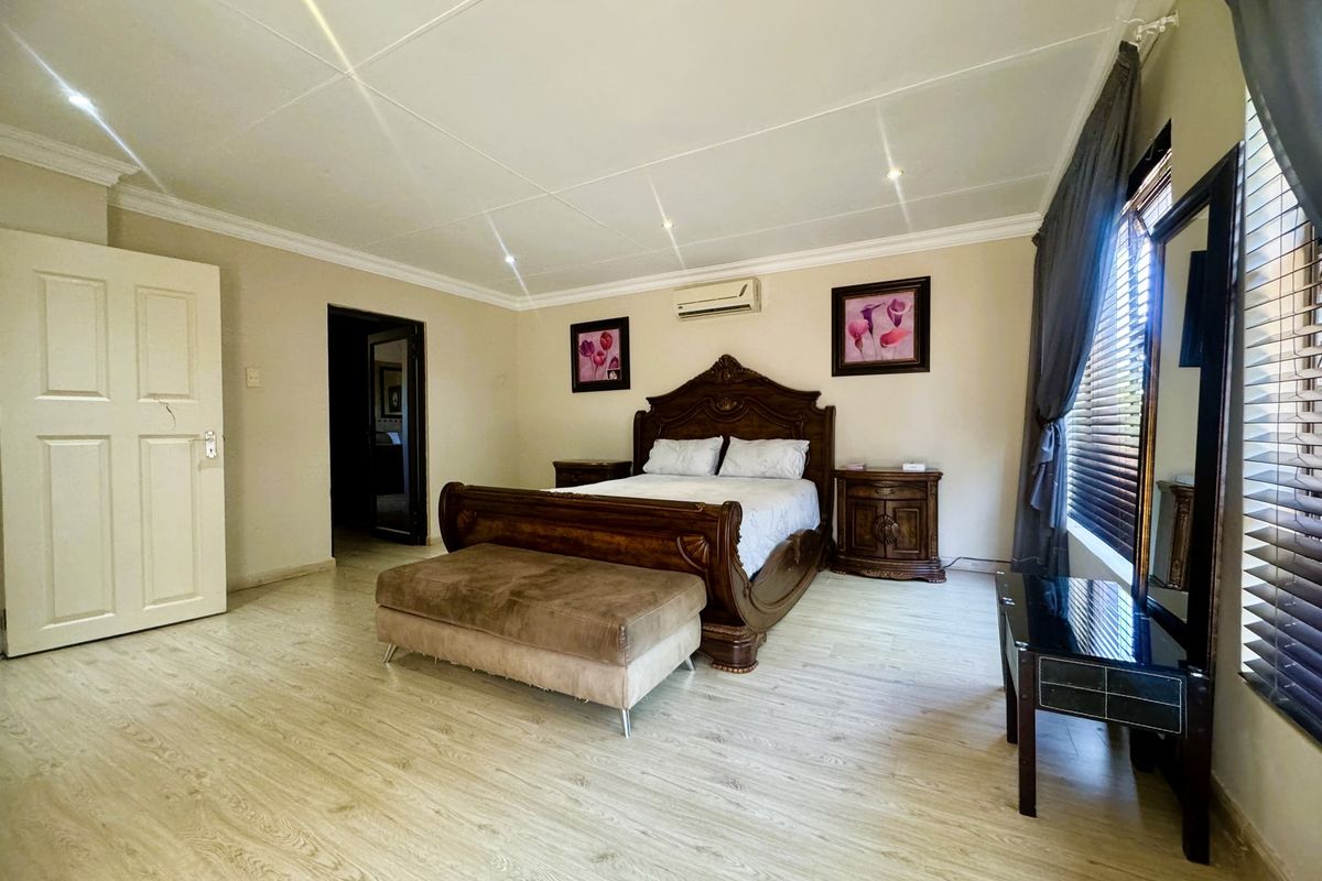 Spacious bedroom featuring light-toned laminate flooring, recessed downlighting, and a wall-mounted air conditioning unit.