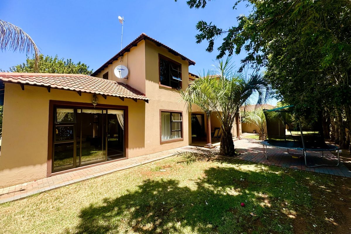Rear view of a two-story house featuring a paved patio area, sliding glass doors, and a well-maintained garden space.