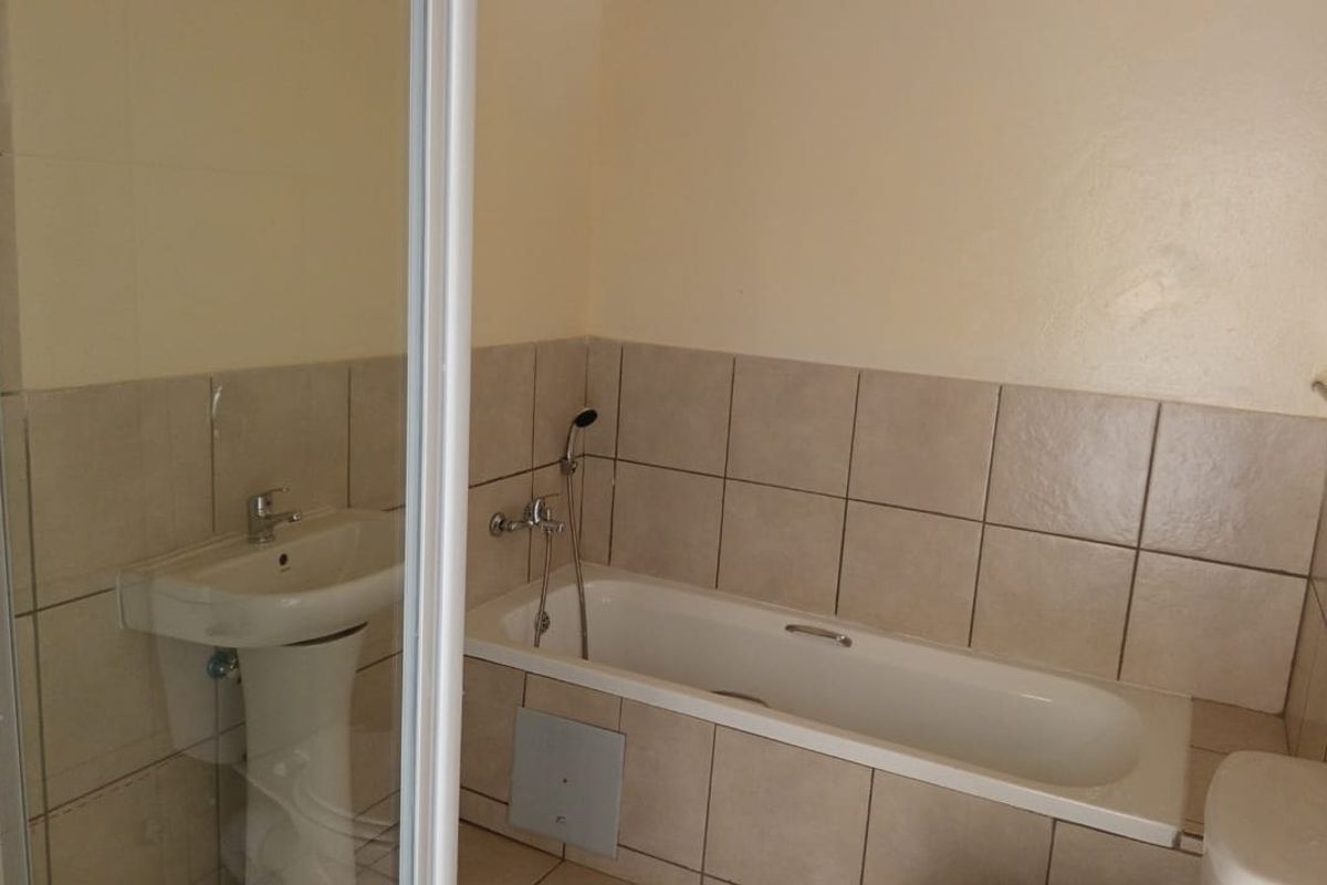 A functional bathroom featuring a bathtub, shower enclosure, and pedestal basin with neutral wall tiling.