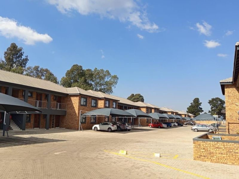 Exterior view of a multi-unit apartment complex featuring face brick construction, tiled roofing, and dedicated shade cloth parking bays for residents.