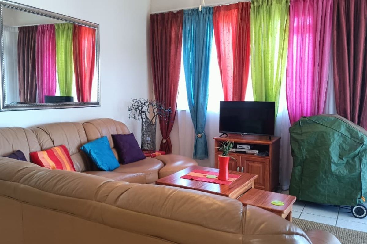 A living room area featuring tiled flooring and large windows dressed with multi-colored curtains.