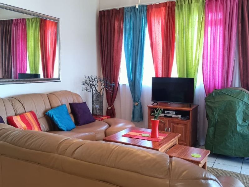 A living room area featuring tiled flooring and large windows dressed with multi-colored curtains.