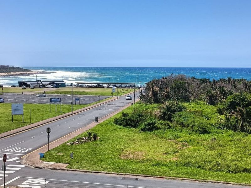 Elevated coastal view overlooking a public road, green space, and the ocean horizon.