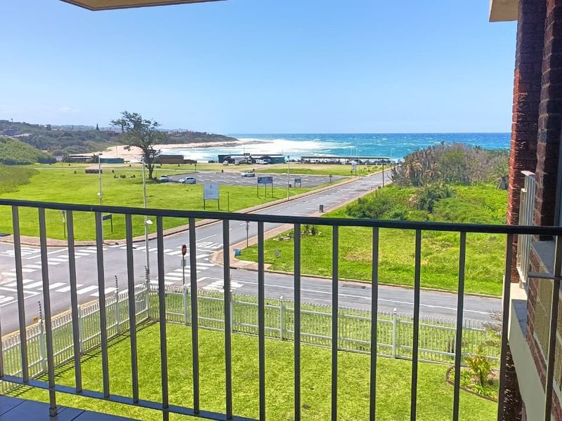 A balcony with a metal balustrade and tiled flooring, offering an expansive view of the coastal landscape and nearby beach.