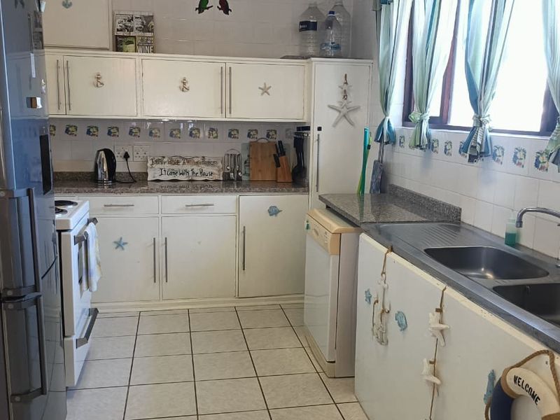 Functional kitchen featuring white cabinetry, granite countertops, double basin sink, and tiled backsplash, offering a practical layout for daily meal preparation.