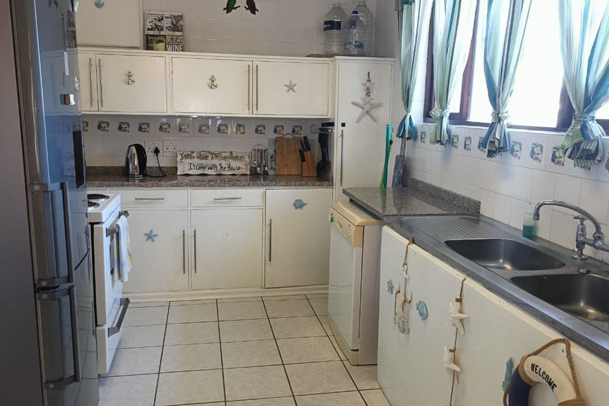 Functional kitchen featuring white cabinetry, granite countertops, double basin sink, and tiled backsplash, offering a practical layout for daily meal preparation.