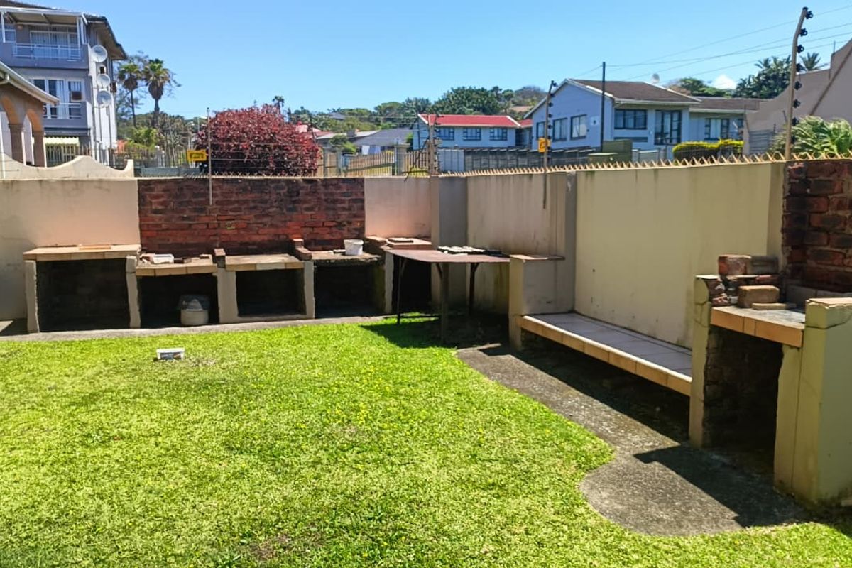 Rear garden area featuring a built-in brick braai, concrete bench seating, and perimeter wall with electric fencing.