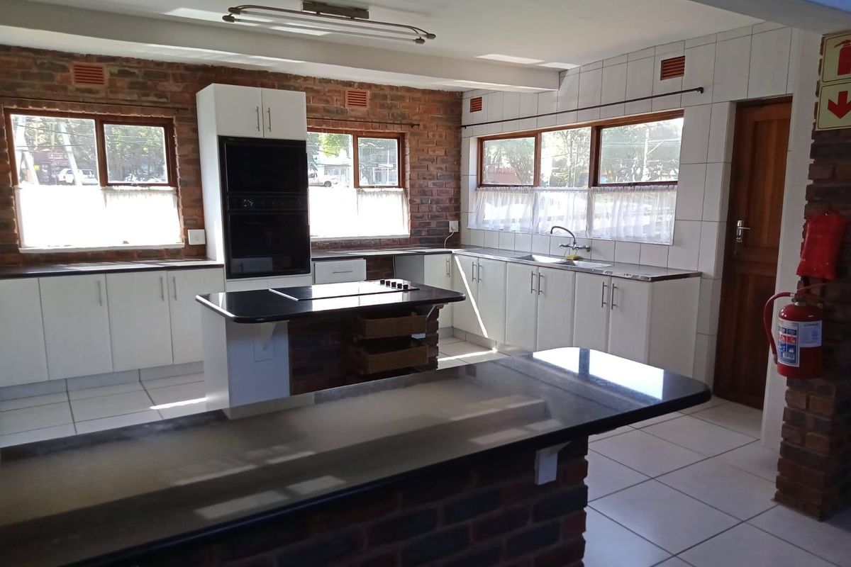 Spacious kitchen featuring exposed brick walls, granite countertops, a central island with a hob, and ample white cabinetry with tiled flooring.