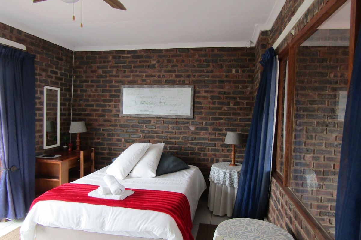 A bedroom featuring exposed brick walls, a ceiling fan, and timber-framed windows, offering a rustic aesthetic.