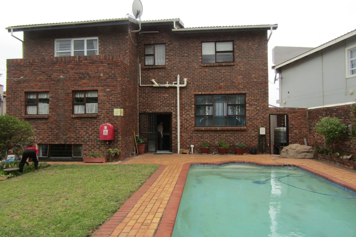 Rear view of a double-story face brick house featuring a swimming pool with paved surround and a small garden area.