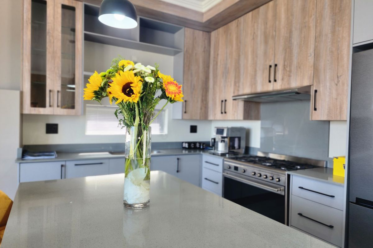 Modern kitchen featuring stone countertops, wood-grain cabinetry, a gas hob with extractor fan, and a sleek glass splashback.