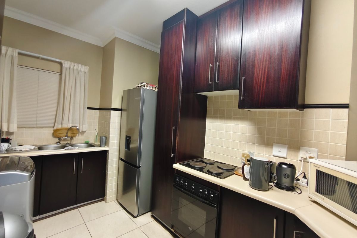 A functional kitchen featuring dark wood cabinetry, tiled backsplash, built-in oven, electric hob, and double basin sink with tiled flooring.