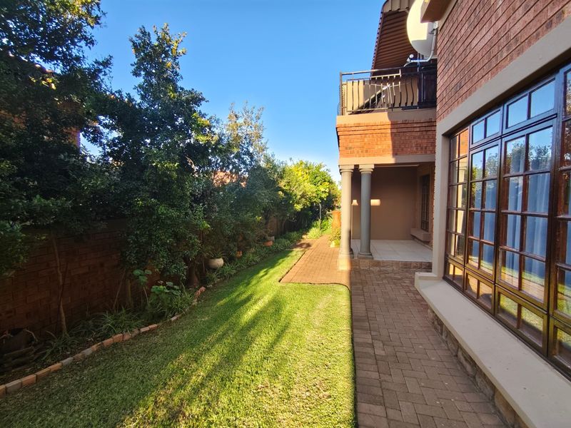 A well-maintained rear garden featuring a brick-paved walkway, a covered patio area, and a balcony with metal railings.