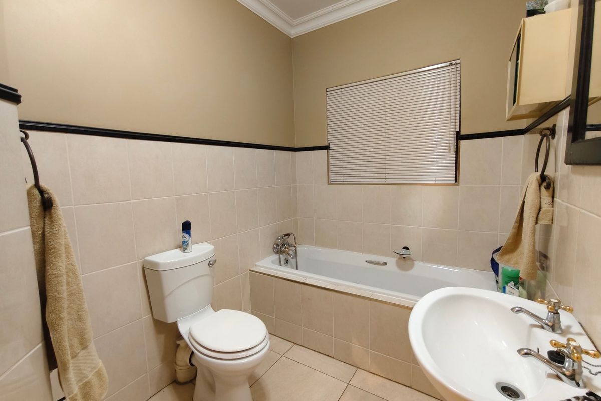 A functional bathroom featuring a built-in bathtub, pedestal basin, toilet, and neutral ceramic tiling with a decorative border.