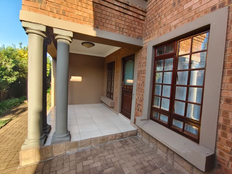 A well-maintained front entrance featuring a covered tiled porch, decorative columns, and classic brick facade with timber-framed windows.