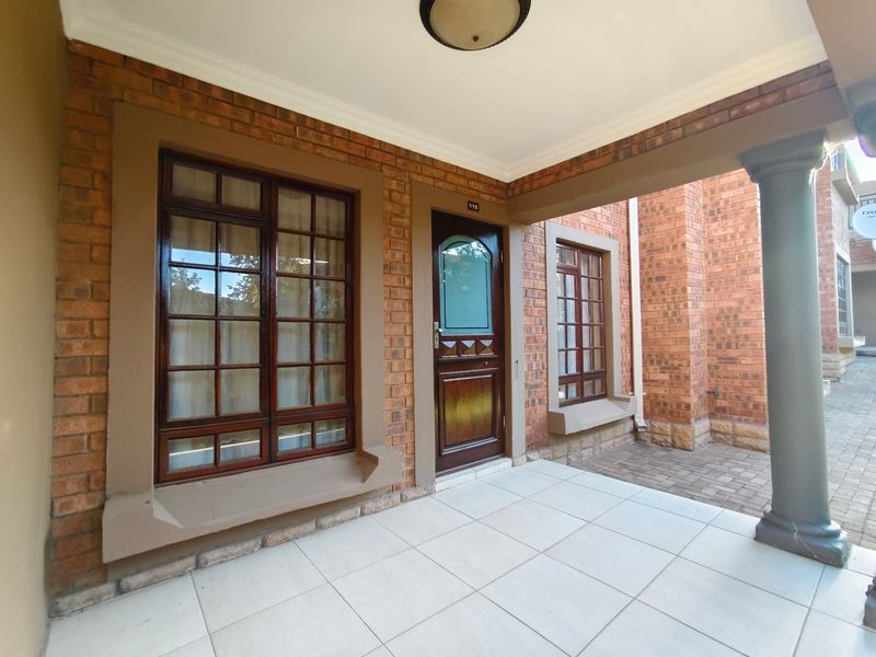 Covered entrance porch featuring brick facade, tiled flooring, and timber-framed windows leading to the main front door.