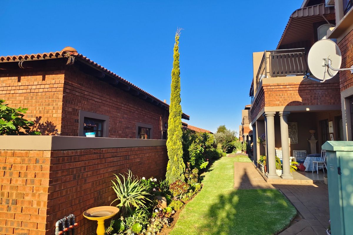 A well-maintained rear exterior view of the apartment complex featuring a brick facade, covered patio area, and landscaped garden with a paved walkway.