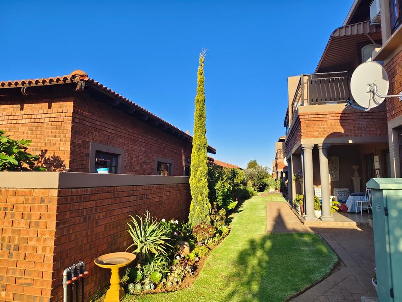 A well-maintained rear exterior view of the apartment complex featuring a brick facade, covered patio area, and landscaped garden with a paved walkway.