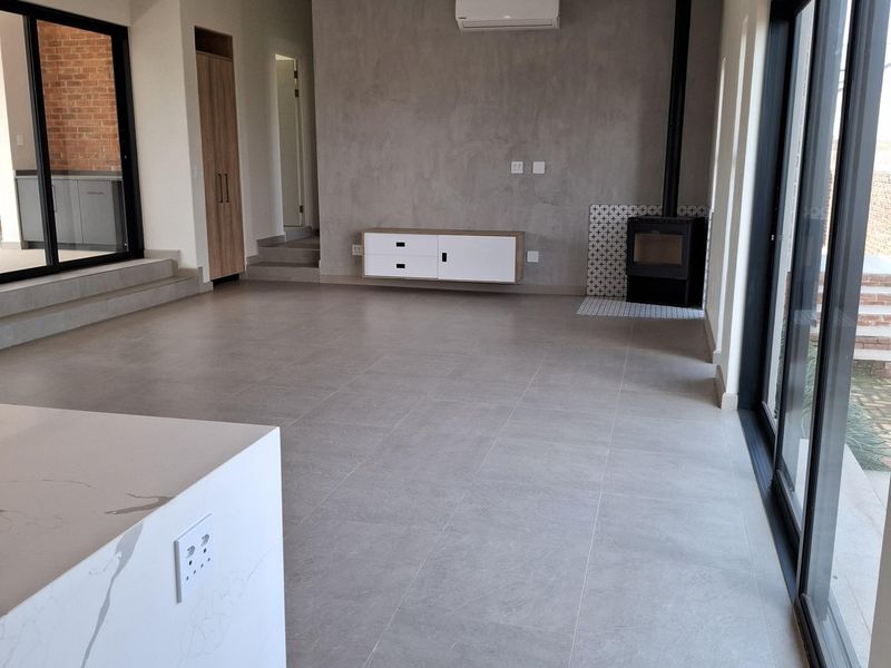 Spacious open-plan living area featuring large format floor tiles, a modern built-in fireplace, split-system air conditioning, and expansive sliding glass doors.