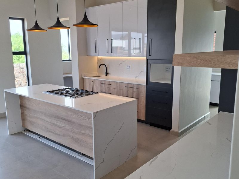 Modern kitchen featuring a central island with a gas hob, stone countertops, two-tone cabinetry, and sleek pendant lighting in an open-plan layout.