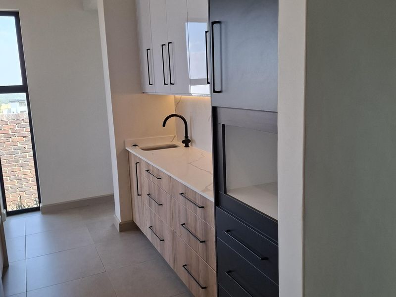 A modern, minimalist scullery featuring sleek two-tone cabinetry, stone countertops, a black mixer tap, and integrated storage solutions.
