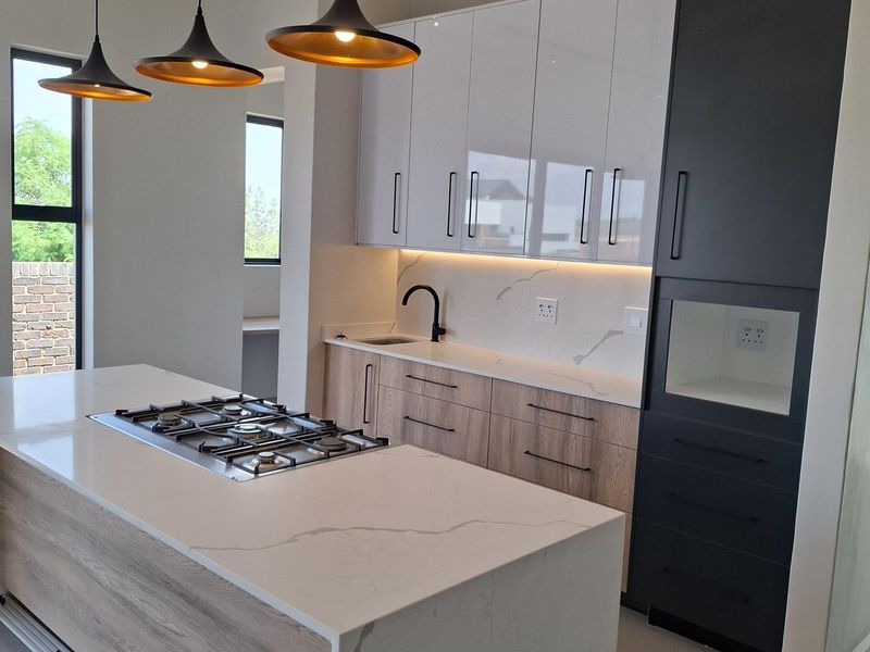 Modern kitchen featuring a central island with a gas hob, quartz countertops, sleek two-tone cabinetry, and contemporary pendant lighting.