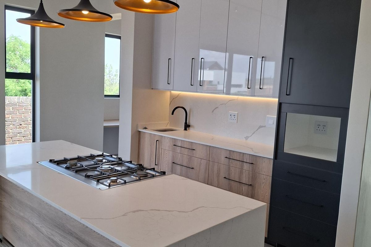 Modern kitchen featuring a central island with a gas hob, quartz countertops, sleek two-tone cabinetry, and contemporary pendant lighting.