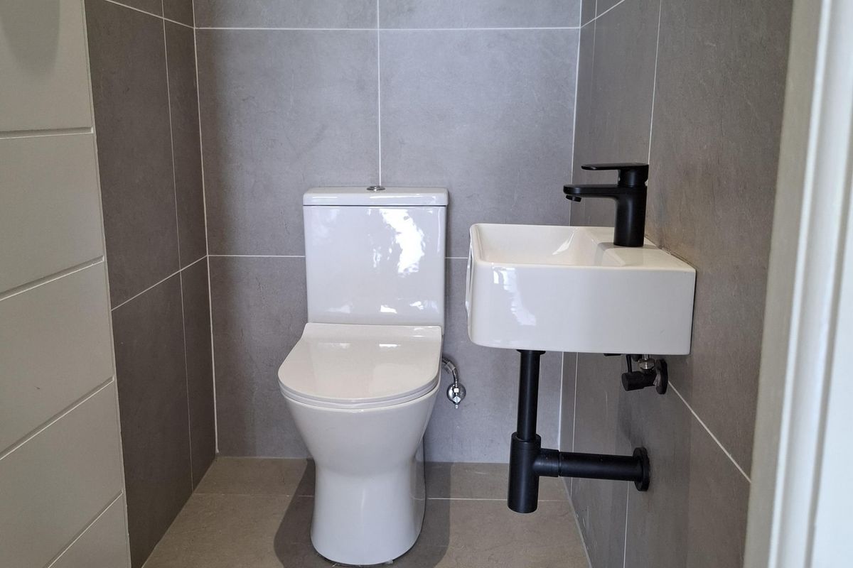 A modern, compact powder room featuring grey floor-to-ceiling tiles, a wall-mounted basin with black tapware, and a white toilet.