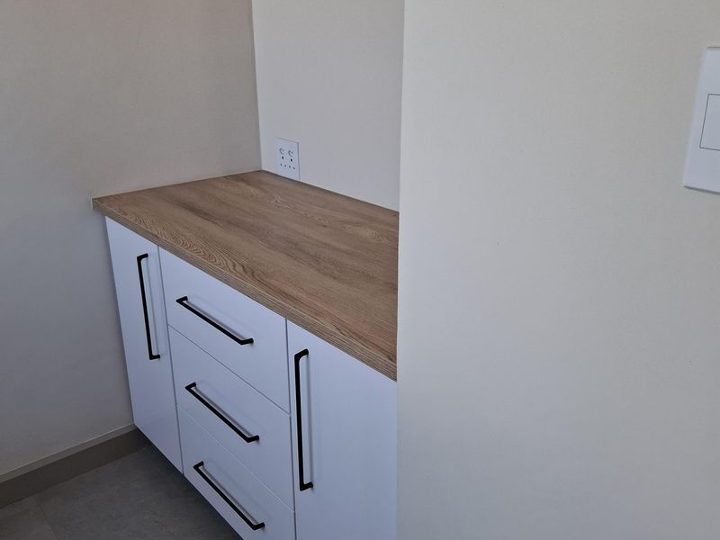 A clean utility space featuring modern white built-in cabinetry with a wood-look laminate countertop and neutral floor tiles.