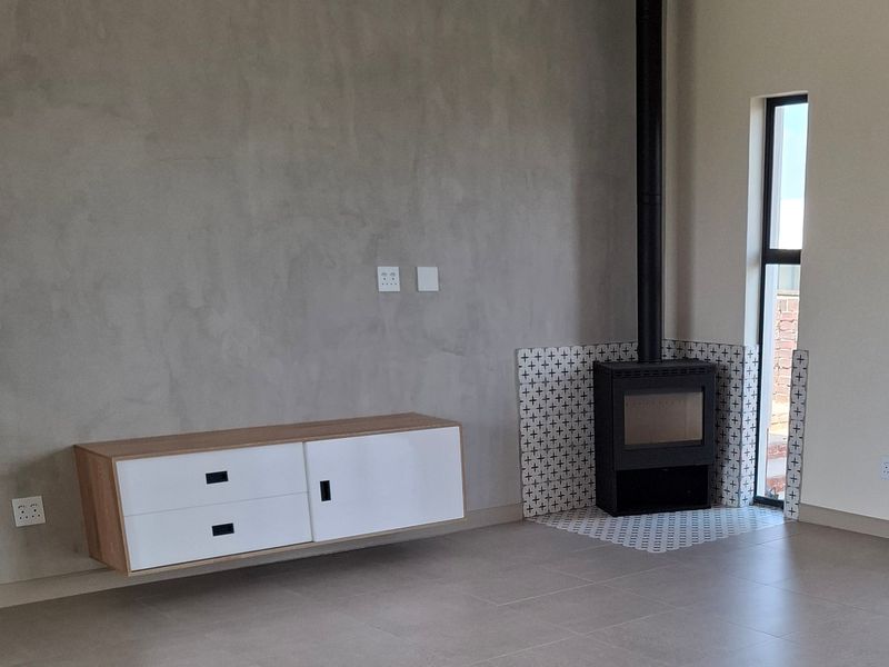 Modern living room featuring a sleek built-in fireplace with decorative tiling, floating cabinetry, and a wall-mounted air conditioning unit.
